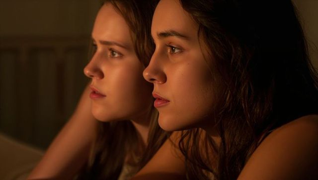 Two young women lying on bed sharing quiet intimate moment warm side-profile portrait