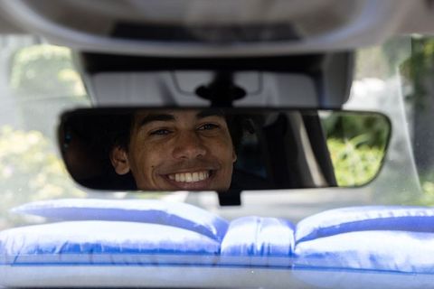 Young man smiling in rearview mirror driving with blue cushions and green background