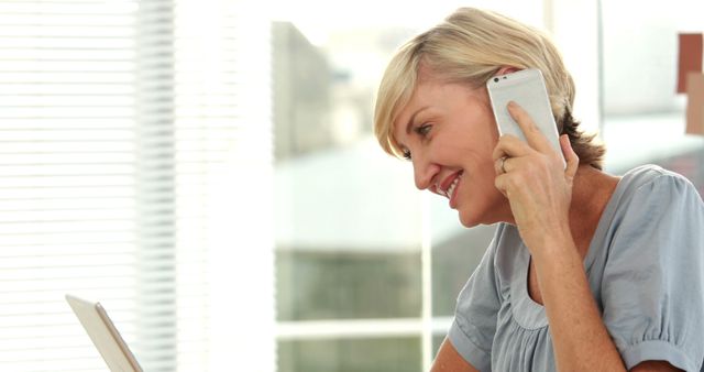 Smiling Senior Woman Talking on Phone and Using Laptop in Bright Office - Download Free Stock Images Pikwizard.com