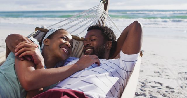 Couple smiling and relaxing on a hammock by the ocean. Perfect for themes related to romantic getaways, beach vacations, leisure time, happiness, romantic relationships, and tropical destinations.