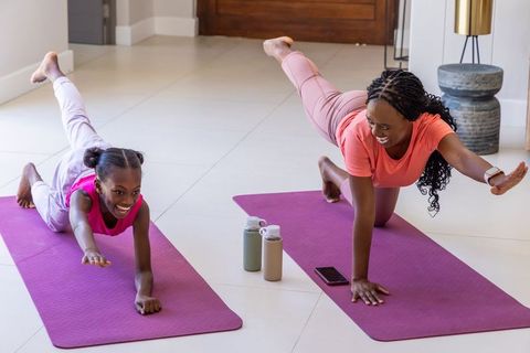 Mother and daughter practicing home yoga balance on purple mats, smiling family fitness