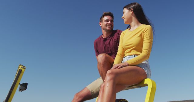 Young couple sitting together outdoors enjoying a sunny day at the beach. Perfect for promoting travel destinations, vacation packages, or lifestyle content.