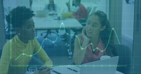 Two Women Discussing Data Insights with Graph Overlay in Office