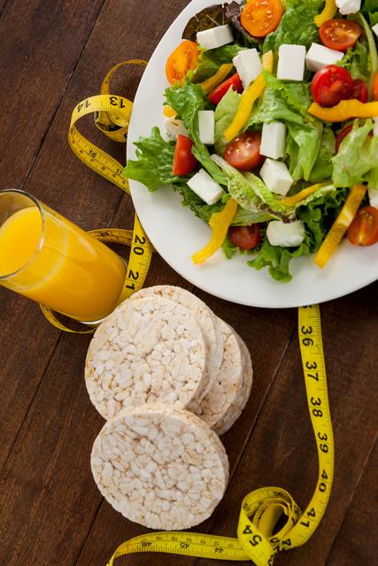 Salad, juice, edible bars and measuring tape on table - diet concept