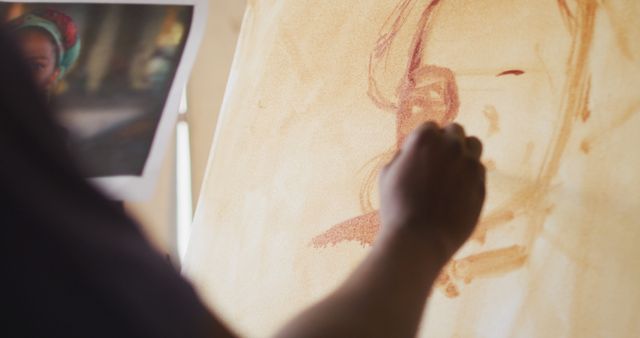 Photo shows an artist drawing a portrait on a canvas in an art studio. The artist's hand and drawing skills are focal points, highlighting the creative process. Useful for topics relating to art, creativity, artistic techniques, and hobby inspirations.