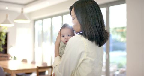 Tender Moment: Mother Cradling Baby in Sunlit Dining Area