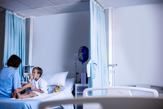 Child using inhaler while sitting in hospital bed, attended by nurse. Suitable for healthcare, medical treatment, pediatric care, and hospital environment themes.