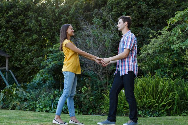 Biracial woman and caucasian man holding hands in garden looking at each other smiling - Download Free Stock Photos Pikwizard.com