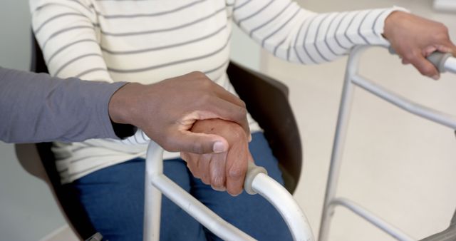 The image depicts an individual offering assistance by holding hands with an elderly person using a walker. This heartwarming image can be used for content related to elderly care, medical assistance, caregiver support, and promoting compassionate care. It is ideal for blogs, websites, or advertisements that focus on healthcare, senior living, or supporting loved ones.