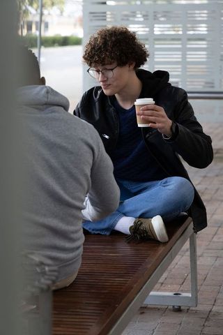 Diverse young men chatting at bus stop drinking takeaway coffee casual urban
