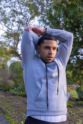 Man Stretching in Backyard with Grey Hoodie for Workout Warm-up