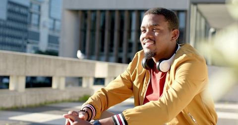 African American man smiling and relaxing outdoors wearing headphones and mustard jacket