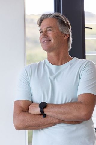 Mature man standing gazing through window wearing mint t-shirt and black smartwatch