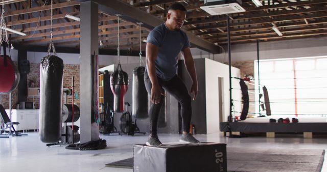 Man performing a box jump exercise in an industrial-style gym setting, highlighting strength and athleticism. Ideal for use in fitness blogs, promotional material for gyms or personal trainers, and workout guides.