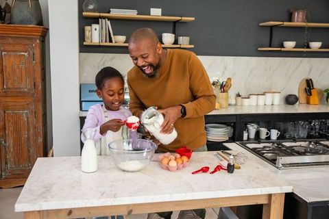 African american father and daughter baking together in modern kitchen sharing laughs