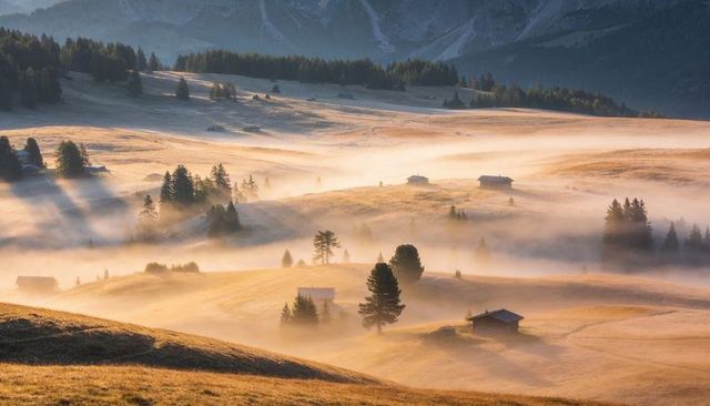 Panoramic golden mist over rolling alpine meadows with wooden cabins and soft sunrise light