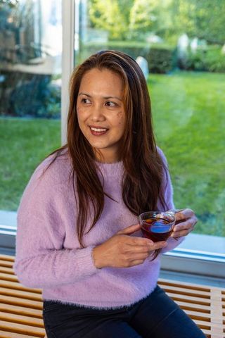 Asian Woman in Lavender Sweater Enjoying Tea by Sunny Window