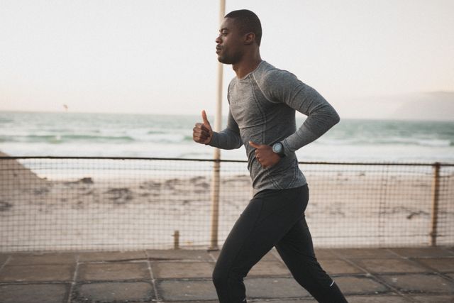 African American man running on a pier by the sea, showcasing a healthy outdoor lifestyle and fitness training. Ideal for use in articles or advertisements promoting fitness, health, and wellness. Suitable for illustrating concepts of determination, morning workouts, and coastal activities.