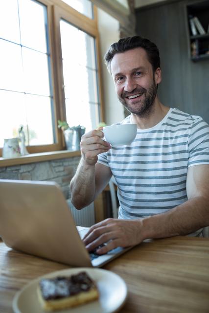 Portrait smiling man using laptop and having a cup of coffee in coffee shop