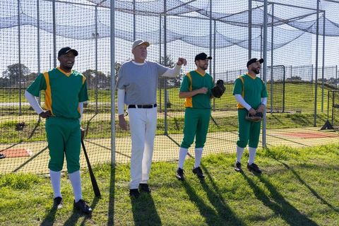 Coach pointing while baseball players adjusting grips during outdoor batting practice