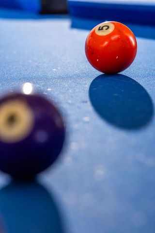 Red #5 pool ball sitting on blue felt with blurred purple ball and glossy reflection