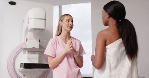 Mammography technologist explaining procedure to patient beside mammogram machine