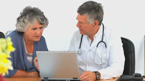 Doctor Consulting Elderly Patient Using Laptop