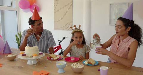 Family celebrating birthday with cake and festive party hats