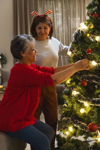 Joyful Friends Decorating Christmas Tree with Ornaments at Home