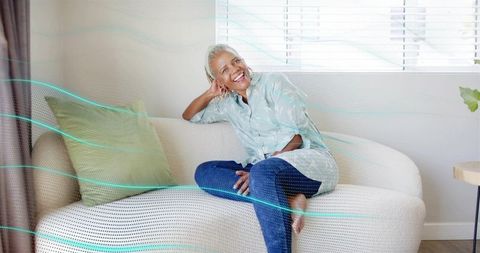 Senior woman smiling and relaxing on modern cream sofa with teal light overlay