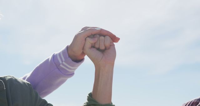 This evocative close-up depicts two people locking pinkies against the backdrop of a blue sky, symbolizing a strong bond, promise, or friendship. Ideal for use in campaigns or blogs about trust, lasting relationships, unity, and the significance of small gestures in significant bonds.