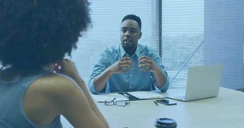 Manager gesturing during job interview at office table with laptop and documents