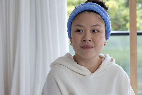 Asian woman wearing white hoodie and blue terry headband relaxing by window