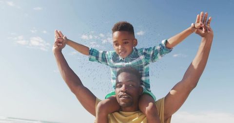Father giving son shoulder ride on sunny beach holding hands and laughing
