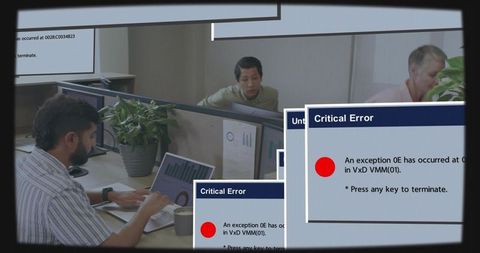 Office worker typing on laptop amid critical error popups in busy modern cubicle workspace