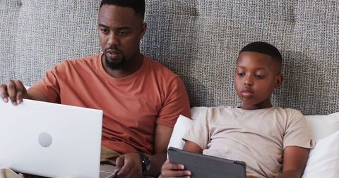 Father and Son Bonding with Laptop and Tablet on Sofa Outdoors