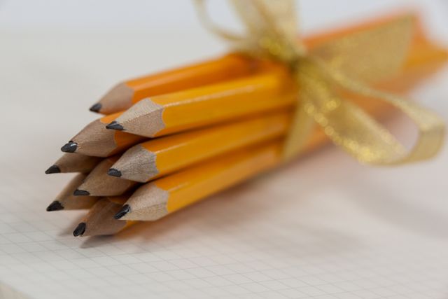 Bunch of yellow pencils tied with a golden ribbon placed on an open notebook. Ideal for back-to-school promotions, educational materials, office supply advertisements, and creative writing themes.