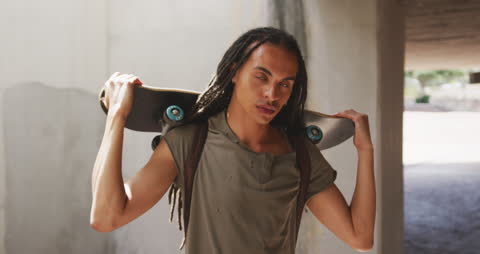 Confident Skater with Dreadlocks Holding Skateboard under Footbridge