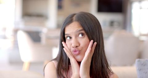 Young woman making funny face with hands on cheeks indoors