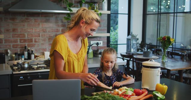 Happy caucasian mother and daughter using laptop and preparing meal together in kitchen. Cooking, communication, family, domestic life and togetherness.