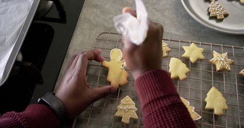 African American Man Decorating Gingerbread Cookies with White Icing on Cooling Rack