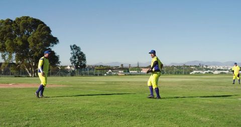 Sunlit Baseball Teammates Wearing Yellow Uniforms and Blue Caps Playing in Outfield