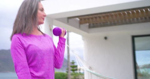 Woman exercising on balcony lifting purple dumbbell overlooking bay