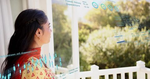 Woman gazing from sunny balcony with teal data overlay, colorful patterned tunic and red scarf