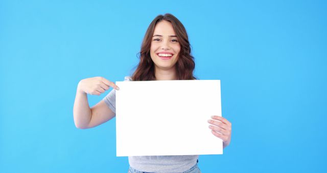 Smiling Woman Holding and Pointing at Blank Sign on Blue Background - Download Free Stock Images Pikwizard.com