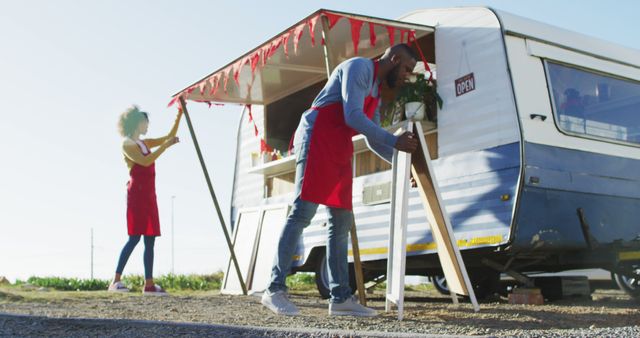 African american couple wearing aprons setting up their food truck on the street. food truck and street food concept