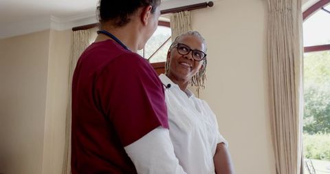 Caregiver communicating with senior woman at home in sunny room