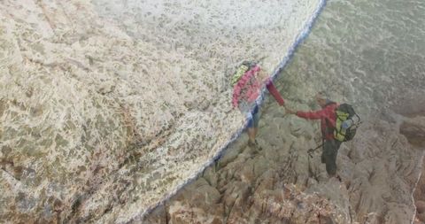 Courageous couple navigating rugged coastal terrain amidst crashing waves