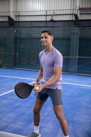 Young athlete practicing padel on covered blue court holding paddle and ball
