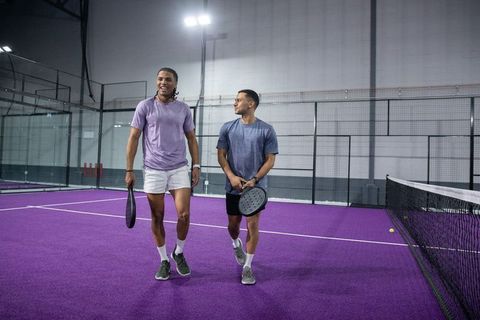 Diverse male friends walking on purple padel court holding paddles smiling and chatting